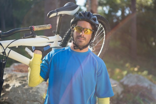 Portrait of male mountain biker carrying bicycle in the forest on a sunny day