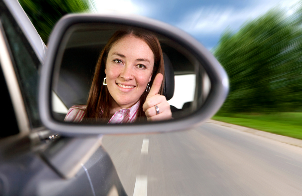 woman driving a car on a road with thumbs up in the mirror