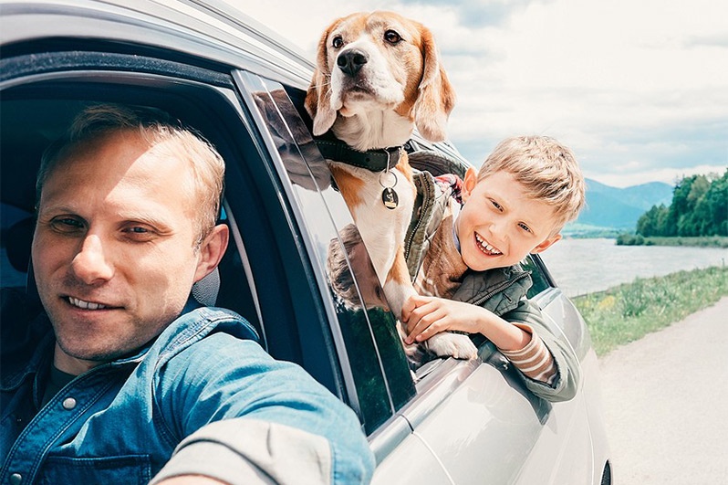 family and dog smiling outside car window